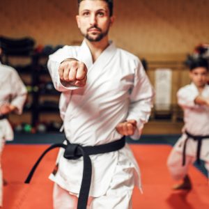 Martial arts karate fighters, master and his disciples in white kimono and black belts hone their skills, fight training in action, workout in gym